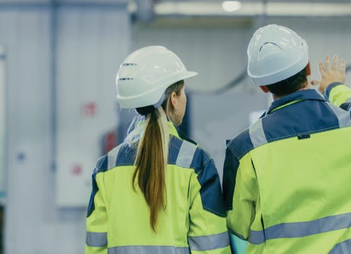 Two business professionals in hard hats and hi vis jackets